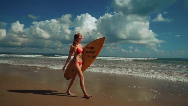 Young slim woman walks on Seminyak beach with a surfboard in Bali