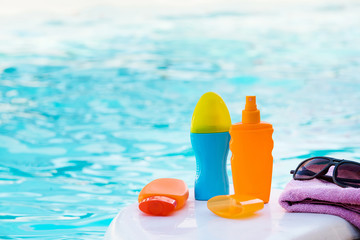 Set for rest: Cream for tanning, sunglasses, towel on blue water background and pink towel