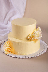 Obraz na płótnie Canvas Beige 2 tiered wedding cake decorated with mastic roses stands on fabric background