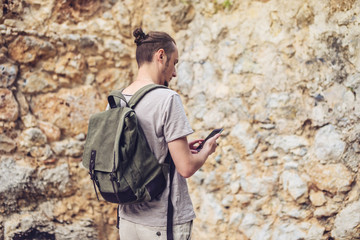 Man traveler with backpack looking at his smartphone on the background of a stone wall