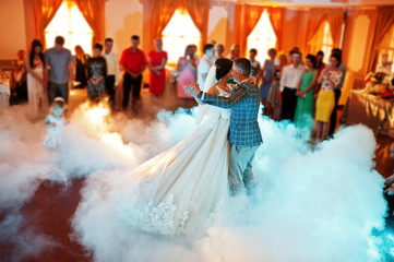 Beautiful wedding couple dancing their first dance in a restaurant with people in the background.