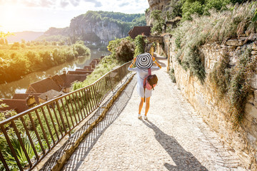 Young woman tourist with backpack and hat walking on the narrow street with beautiful landscape view in the famous La Roque Gageac village in France