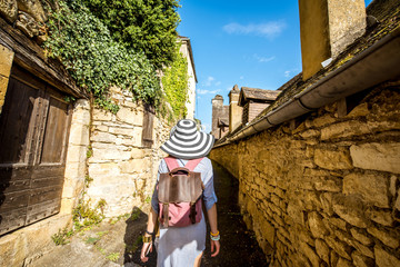 Young woman tourist with backpack and hat walking on the narrow street in the famous La Roque...