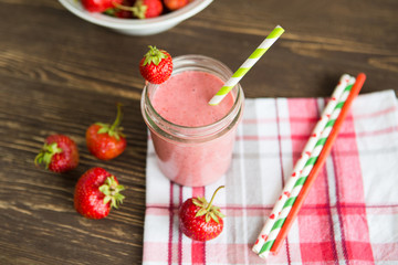 Healthy strawberry smoothie in mug with checkered cloth against rustic wood.