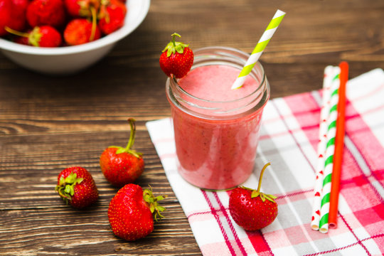 Healthy strawberry smoothie in mug with checkered cloth against rustic wood.