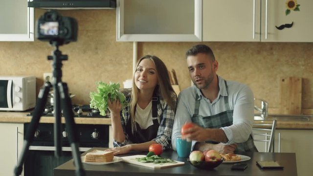 Young attractive couple bloggers shooting video food blog about cooking on dslr camera in the kitchen