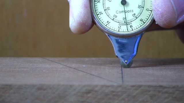 A vintage compass map measuring gauge is used to verify dimensions on maple board for cutting.  Macro shot from slight high angle looking down with wood background.