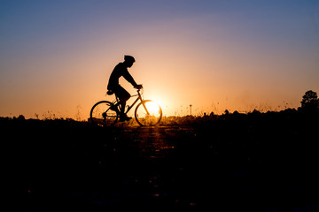 Silhouette of cyclist riding on a bike on road at sunset.