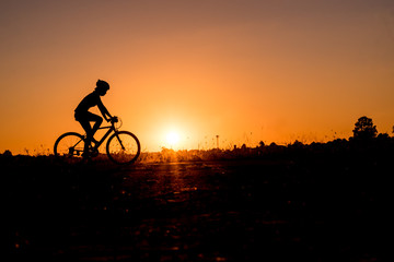 Fototapeta premium Silhouette of cyclist riding on a bike on road at sunset.