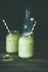 Cold refreshing iced coconut matcha latte drink in glass jars. Selective focus, copy space, dark table background. Clean eating, healthy, vegetarian, vegan, alkaline diet, dairy free food concept