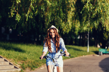 Young pretty woman posing on the nature with bike in summer sunshine