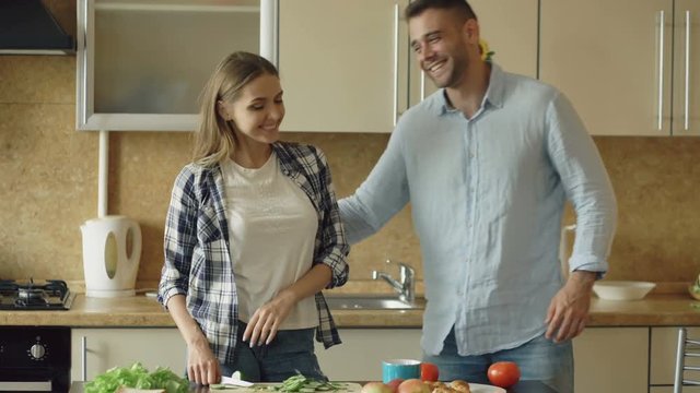 Happy young couple in the kitchen. Attractive woman cooking breakfast and cuff her boyfriend who want to taste food