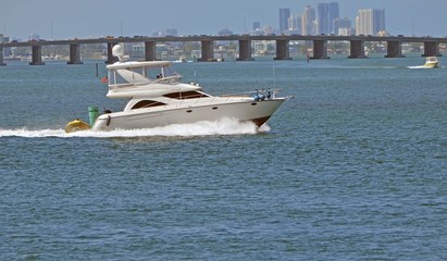 Obraz premium Upscale fishing boat cruising on the florida intra-coastal waterway with a Julia Tuttlle Causeway bridge and Miami high-rise buildings in the background