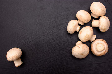 Whole mushrooms champignons whole lie on a black stone slate, background