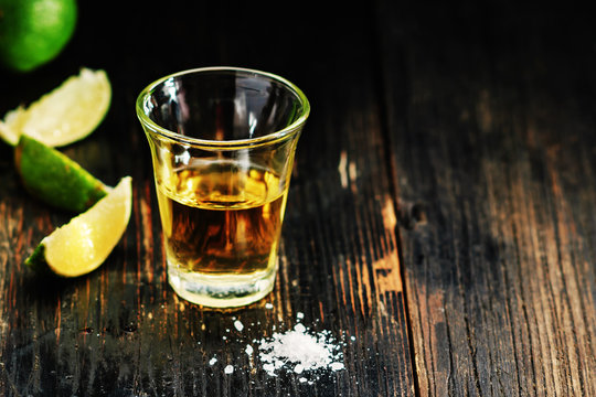 Golden tequila shots with sea salt, juicy lime on vintage black wooden board, toned, selective focus, copy space.
