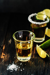 Golden tequila shots with sea salt, juicy lime on vintage black wooden board, toned, selective focus, copy space.