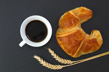 French croissant and coffee on black slate stone plate for morning breakfast or break time with copy space