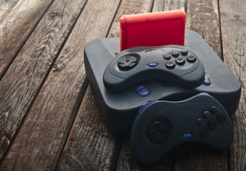 Vintage game console with gamepads and cartridge on a wooden table.   © splitov27