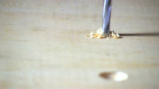 A seconds hole is drilled into pine board with cordless drill & countersink bit.  Sawdust is then blown away.  Macro shot from slight high angle looking down.  Audio included in clip