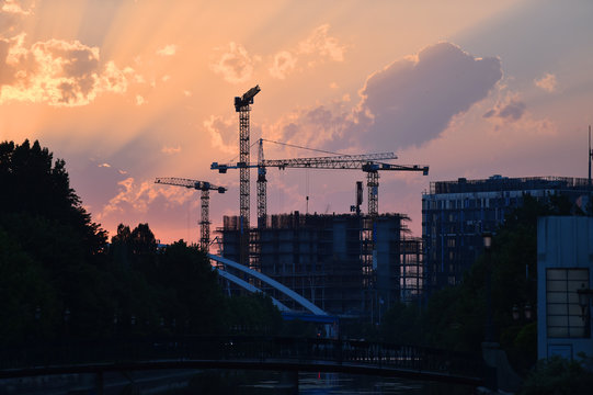 Construction cranes silhouetted against sunset sky