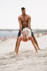 Fototapeta na wymiar Atractive man and woman friends having fun on beach and doing some fitness workout