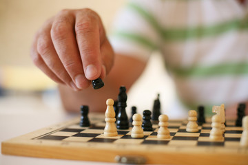 Senior man playing chess, close-up of hand.