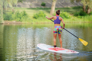 Young woman on a board with an oar. Side view - the concept of harmony with nature, a free and healthy lifestyle, supernumerary staff