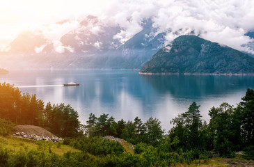 White ship on the background of mountains and forest covered with clouds in cloudy weather in Norway.