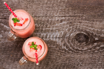 Glass of strawberry yogurt or smoothie with mint leaves on old wooden background with copy space for your text. Top view