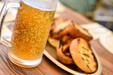 Sweaty mug of cold beer on a hot summer day, with bubbles visible, on a restaurant table with oiled bread in the background