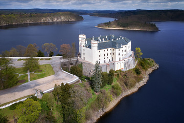 Aerial view on czech romantic, gothic chateâu Orlik, situated on rock outcrop above  Orlik reservoir in beautiful spring nature. Romantic,royal Schwarzenberg castle above water level. Czech landscape. - obrazy, fototapety, plakaty