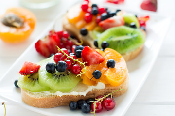 Fruit dessert sandwiches with ricotta cheese, kiwi, apricot, strawberry, blueberry and red currant on white wooden table. Selective focus