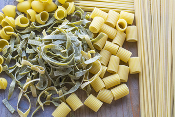 Several sorts of raw green and yellow pasta are on the wooden background
