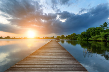 Wooden path bridge over lake at stormy dramatic sunset - Powered by Adobe