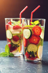 Cold and refreshing infused detox water with strawberry and cucumber in glass on black background.