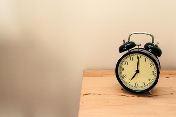 black vintage retro alarm clock times at 7 o'clock morning on wooden table, selective focus, copy space, vintage color tone