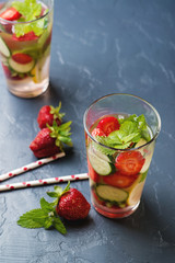 Cold and refreshing infused detox water with strawberry and cucumber in glass on black background.