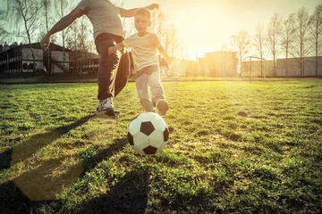 Tuinposter Father and son playing together with ball in football under sun © Andrii IURLOV
