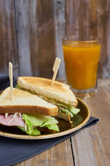 Club sandwich with cheese, ham, lettuce on plate and glass of Sea-buckthorn berries juice