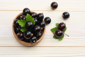 black currant in wooden bowl with green leaf on white wooden background. top view with copy space