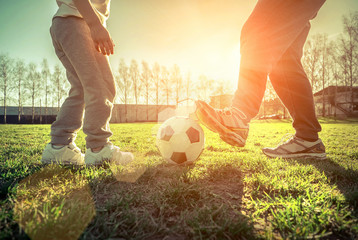 Father and son playing together with ball in football under sun