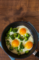 Fried eggs with broccoli in a iron frying pan on the brown wooden table background. with copy space. top view.