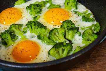 Fried eggs with broccoli in a iron frying pan on the brown wooden table background.