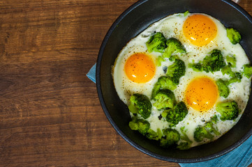 Fried eggs with broccoli in a iron frying pan on the brown wooden table background. with copy space. top view.
