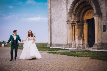 Fototapeta premium gorgeous wedding couple . The happinest brides embracing near castle. Groom and bride embrace on a background of the castle. very lucky in love wedding day. The groom holds the bride on hands