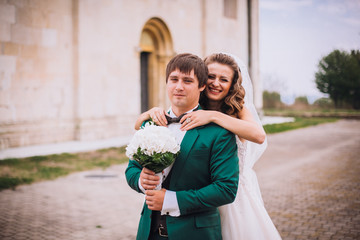 Fototapeta premium gorgeous wedding couple . The happinest brides embracing near castle. Groom and bride embrace on a background of the castle. very lucky in love wedding day. The groom holds the bride on hands