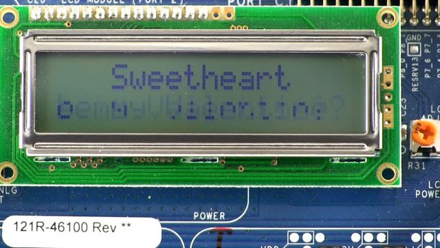 A 2x16 character LCD display screen showing "Sweetheart" in static letters on first row and "Will you be my Valentine?" in scrolling marquee letters on second row