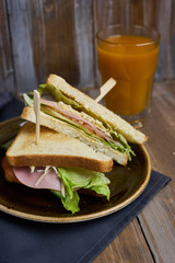 Club sandwich with cheese, ham, lettuce and toast bread on plate and glass of Sea-buckthorn berries juice on wooden table