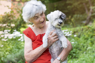 Senior woman hugging her poodle dog in a park with blooming margaritas