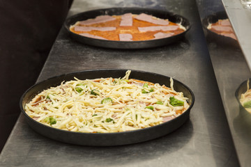 Two black metal baking sheets with raw pizza.